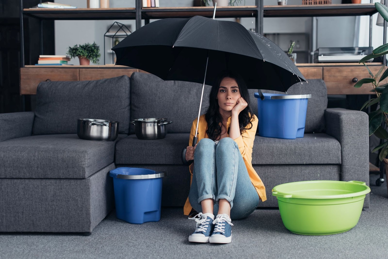 Pensive brunette girl sitting on floor with umbrella because she has a water leak