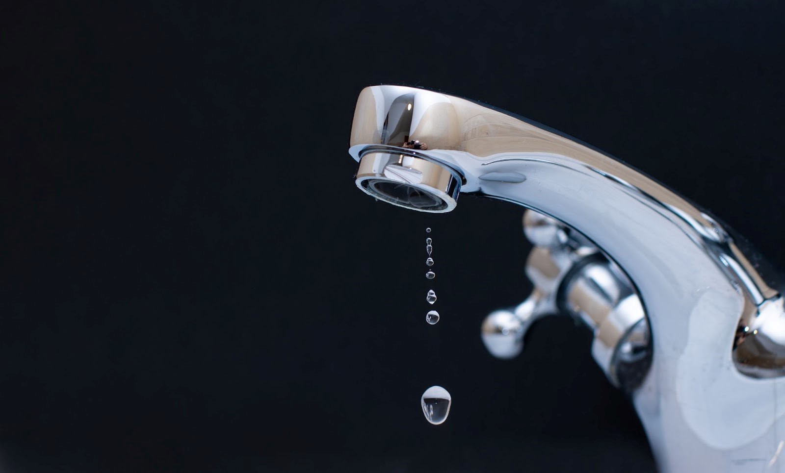 Water dripping from a faucet on a black background