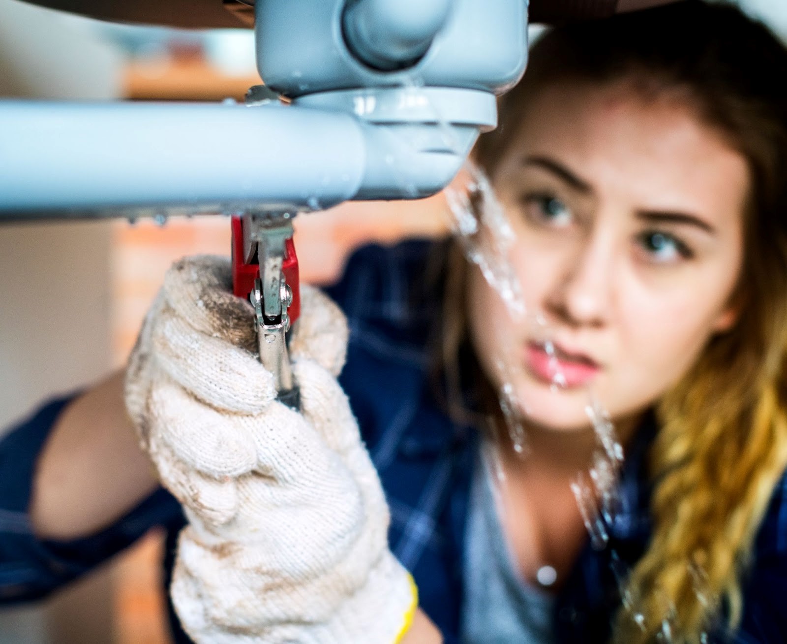 Woman wearing work gloves, holding tool, trying to fix a burst sink pipe