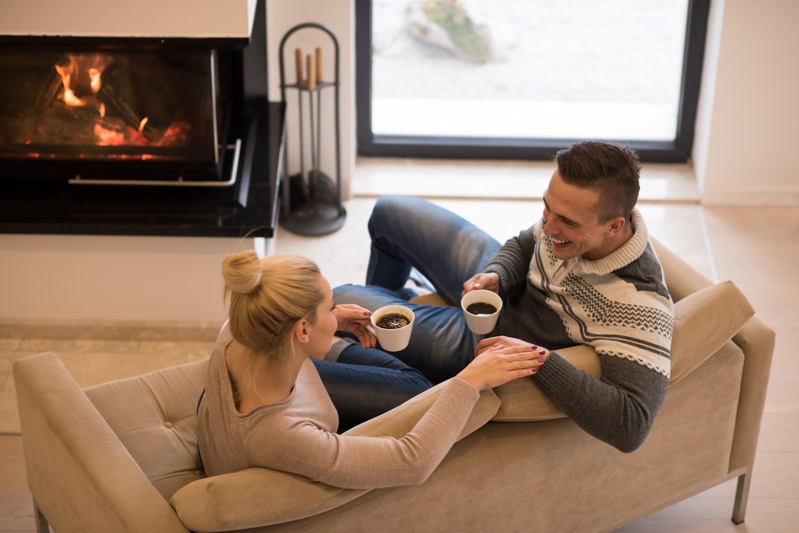 Young couple on a couch with coffees next to a fireplace