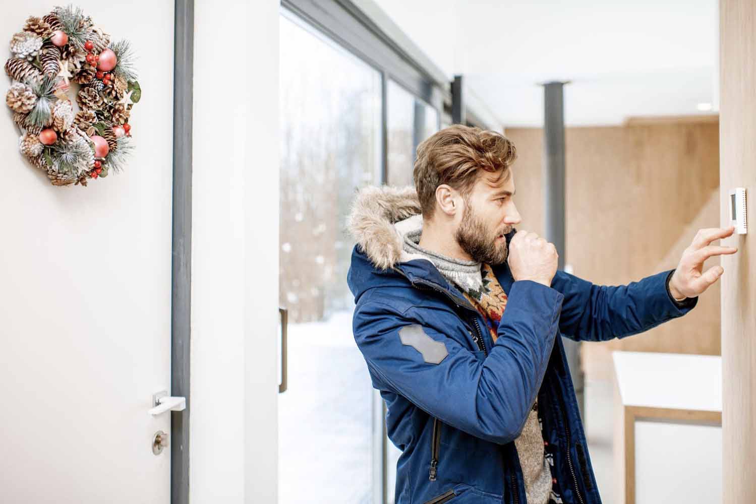 Man in blue parka is cold and needs to adjust his thermostat too often. Time for an upgrade to a smart thermostat.