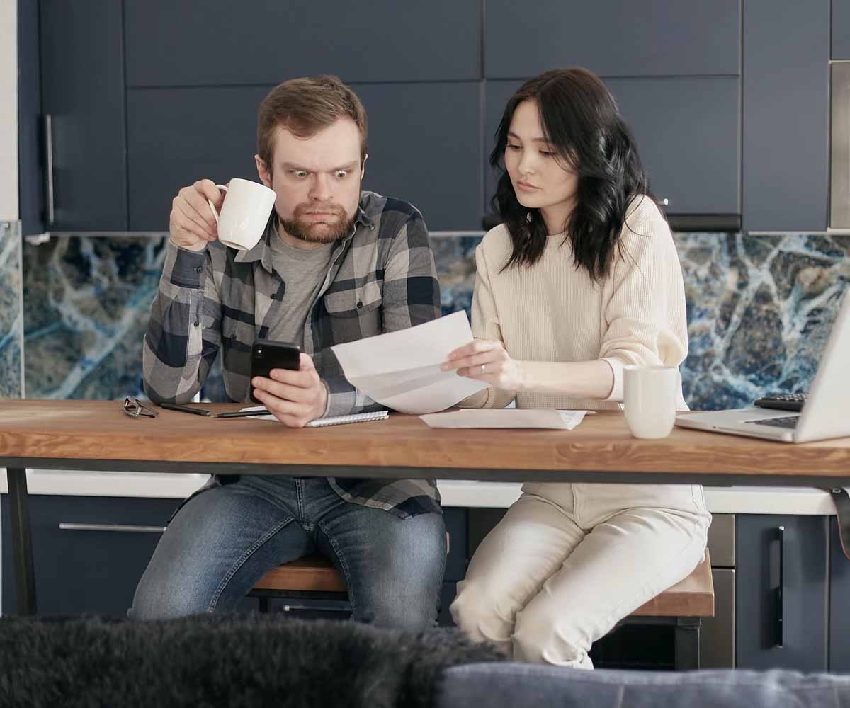 A shocked man looking at his high utility bills while Holding a Coffee and Phone