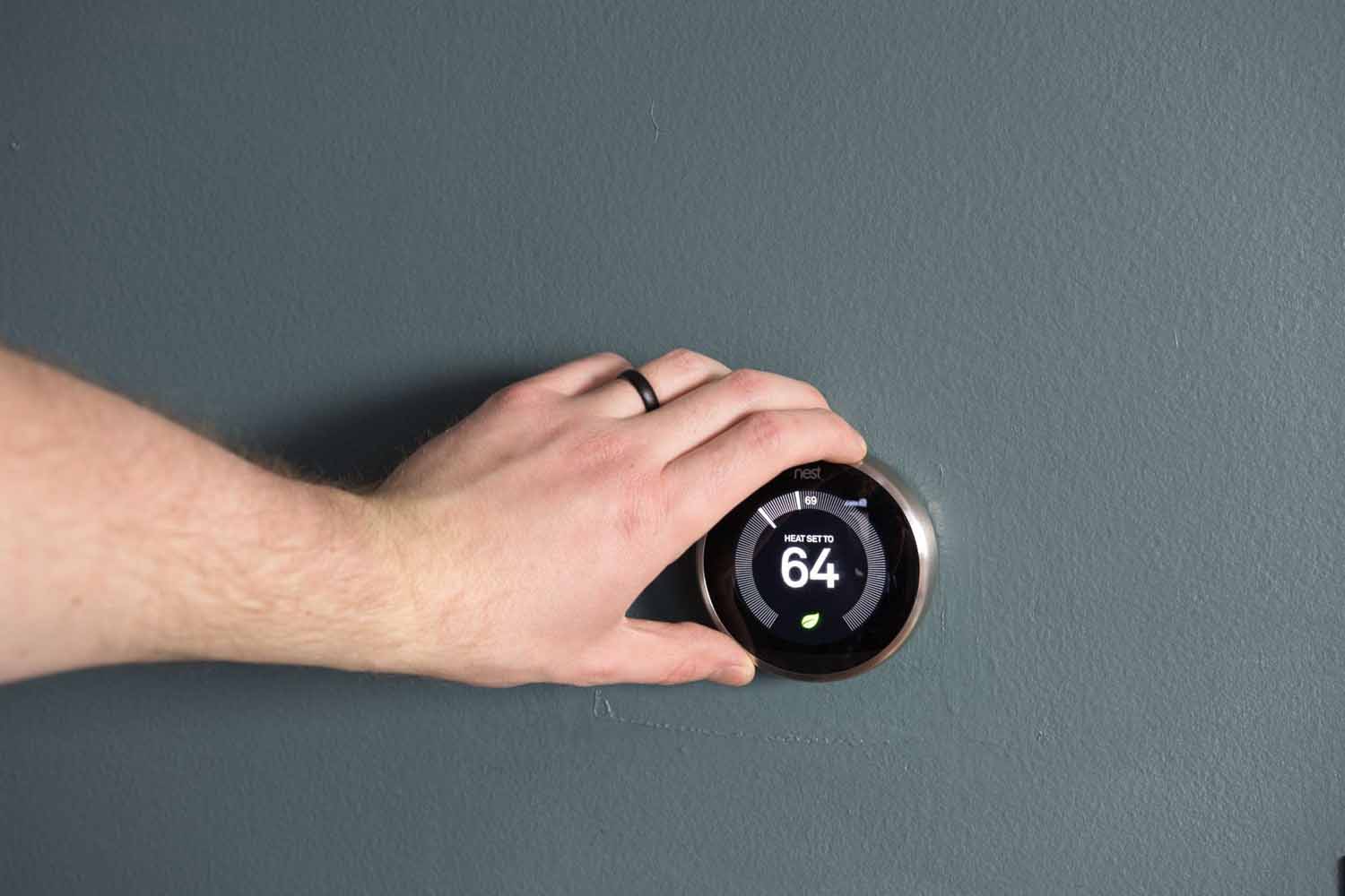 Hand adjusting a smart thermostat to save money