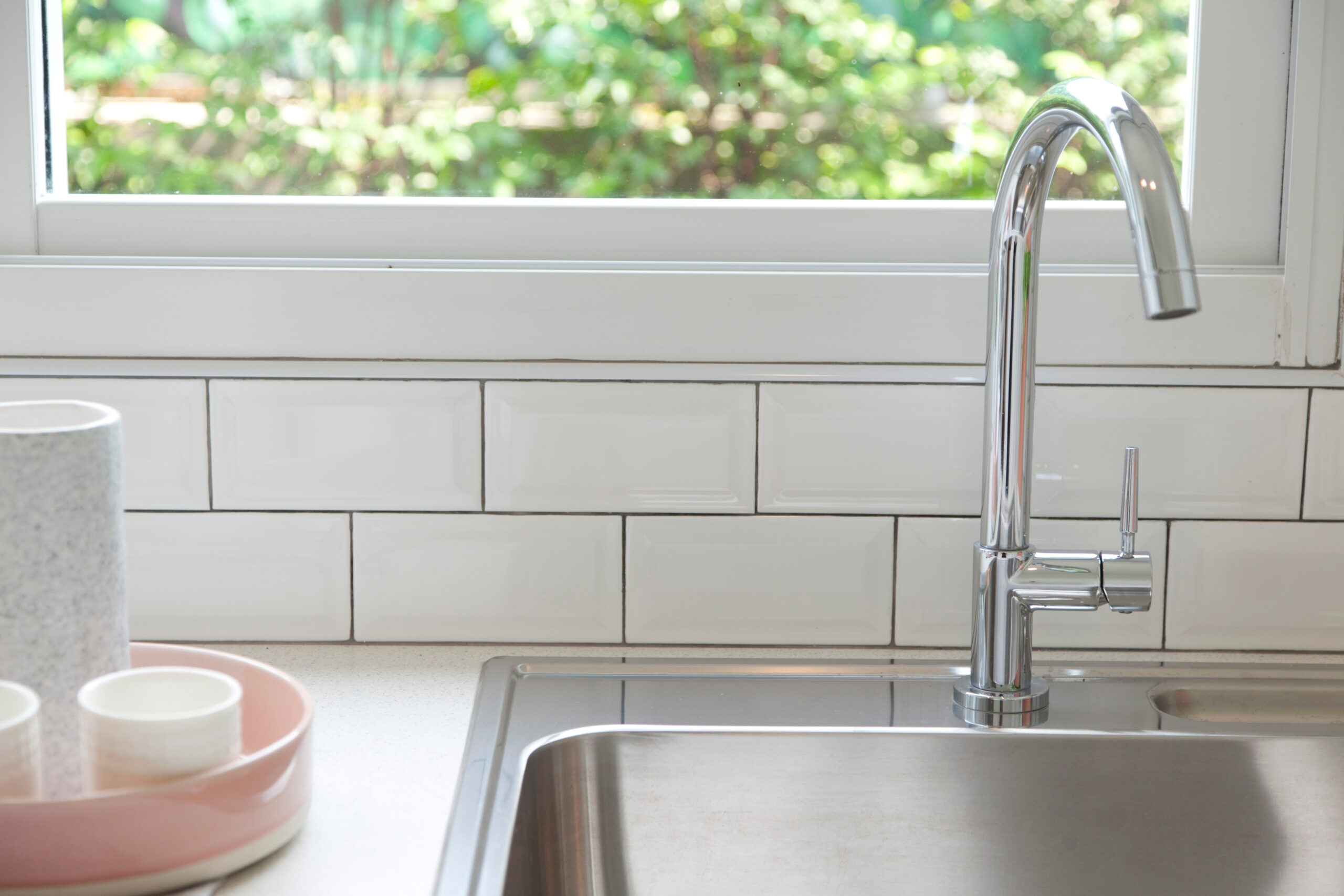 Upgraded kitchen sink faucet with window and white tile backsplash.