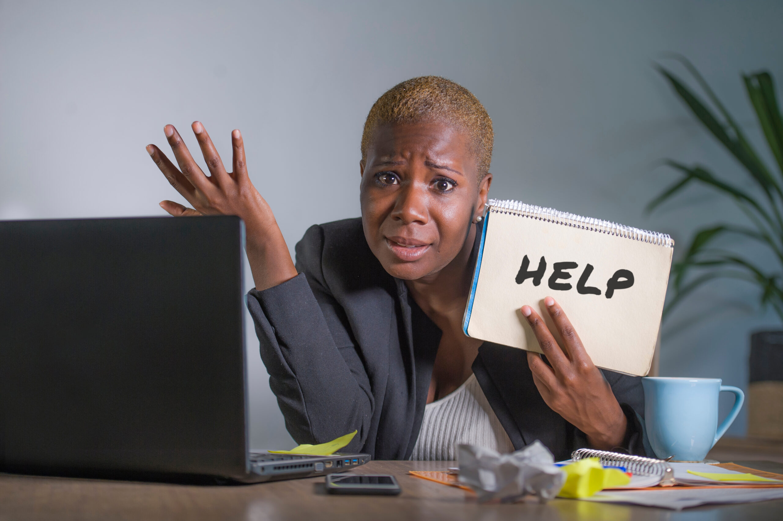 Confused woman with a laptop holding up a notebook that says ‘help’ while she tries to figure out which HVAC system is right for her house