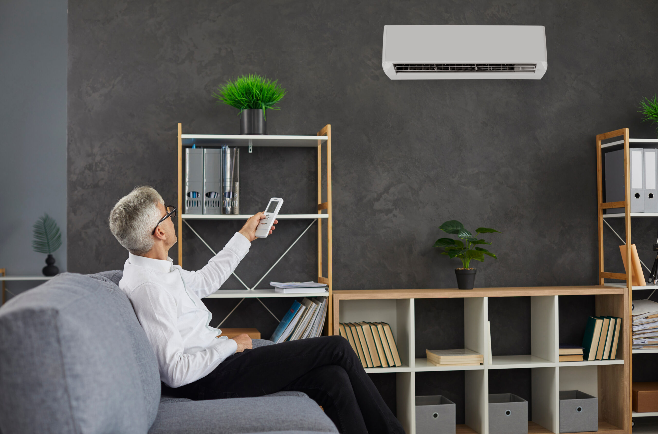 Older man sitting on a couch uses remote control to turn on ductless mini split HVAC