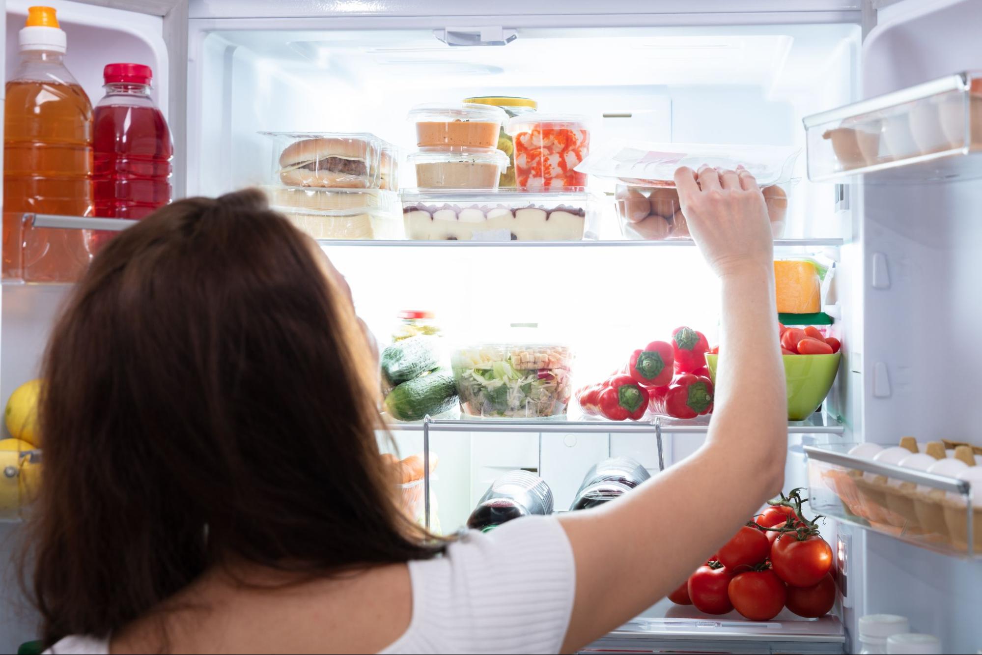 Woman reaching into a well-lit, well-stocked refrigerator