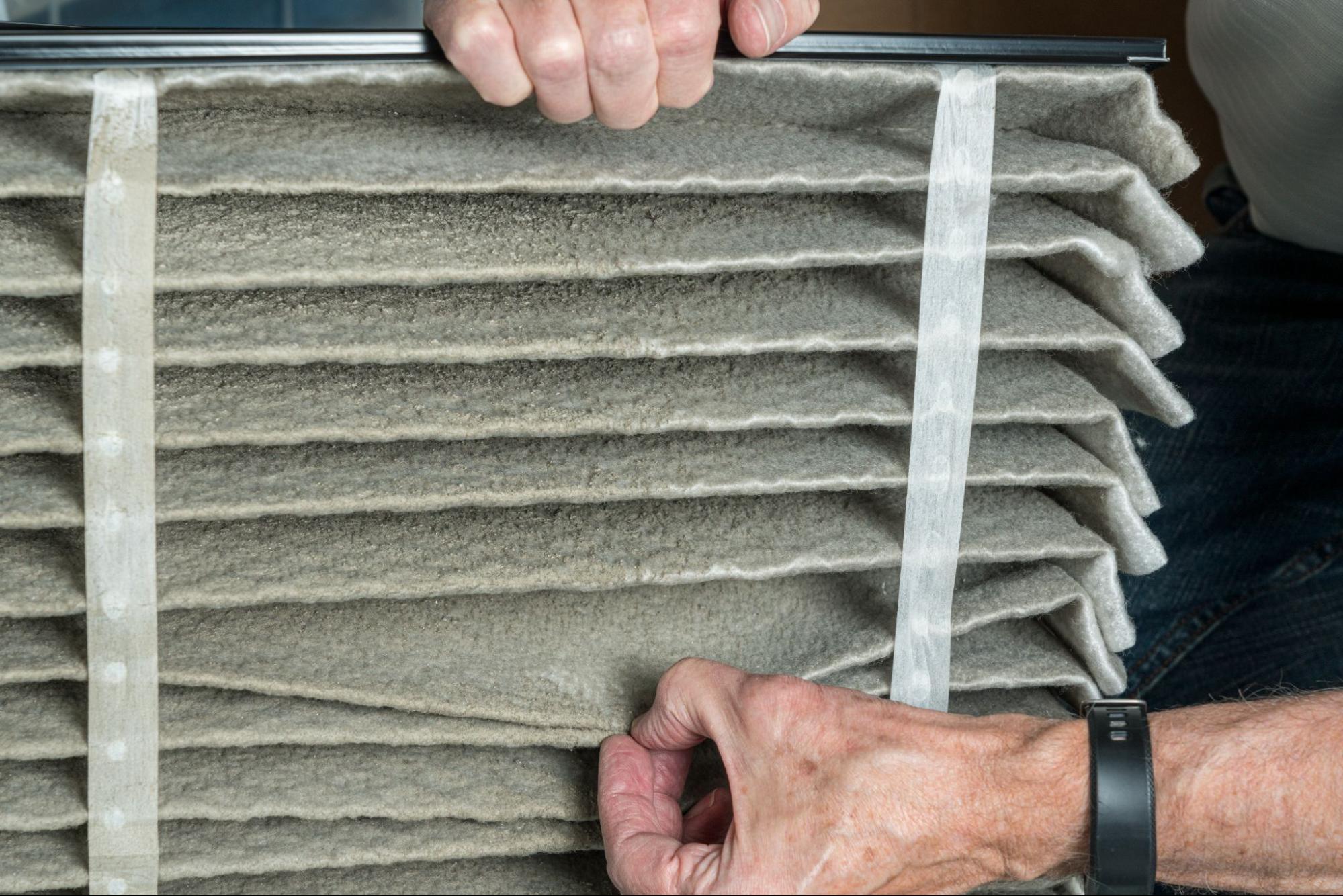 Man looking at the dust in the folds of a very dirty air filter of a HVAC furnace system