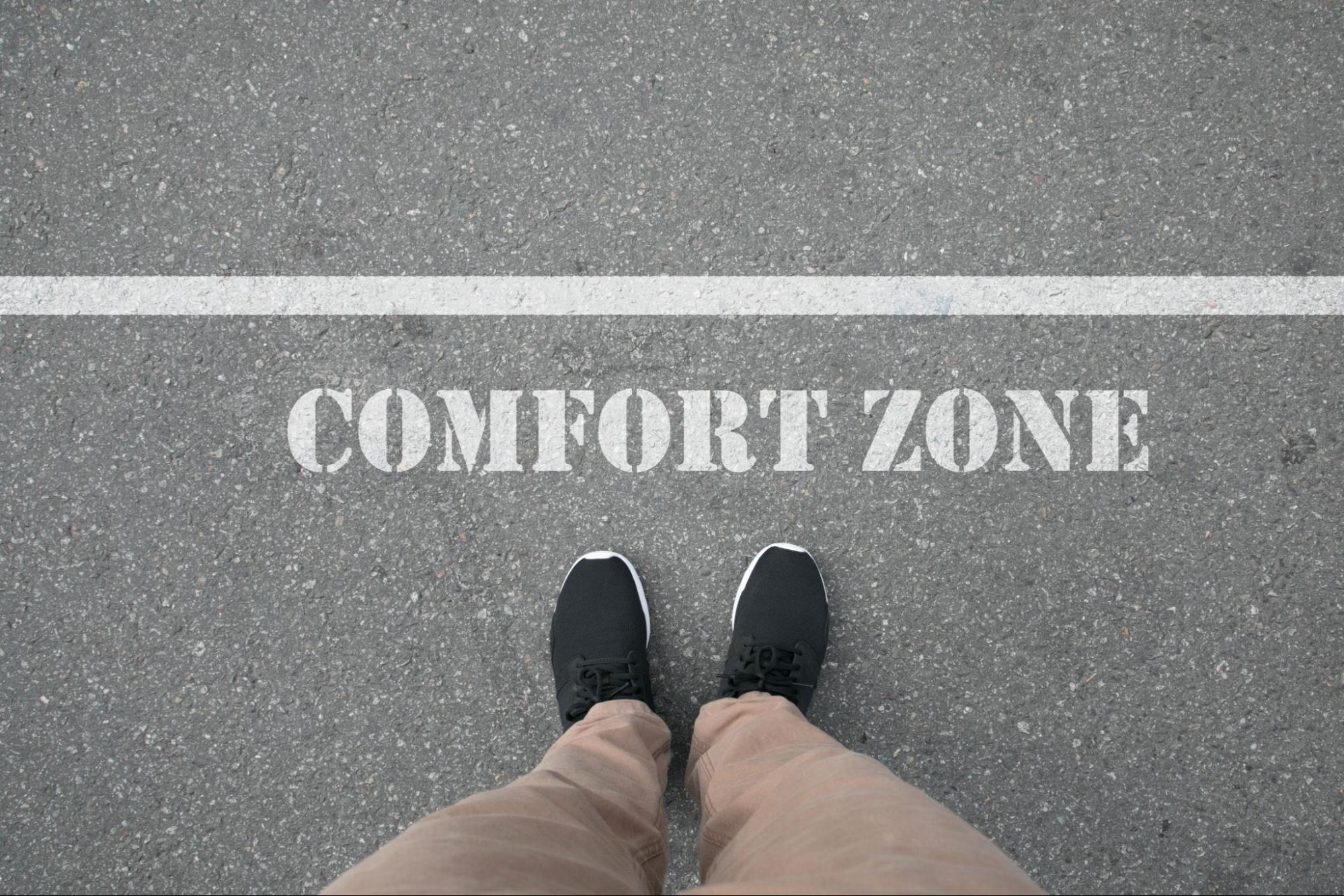Shoes standing on an asphalt road in front of the words ‘comfort zone’ stenciled in white