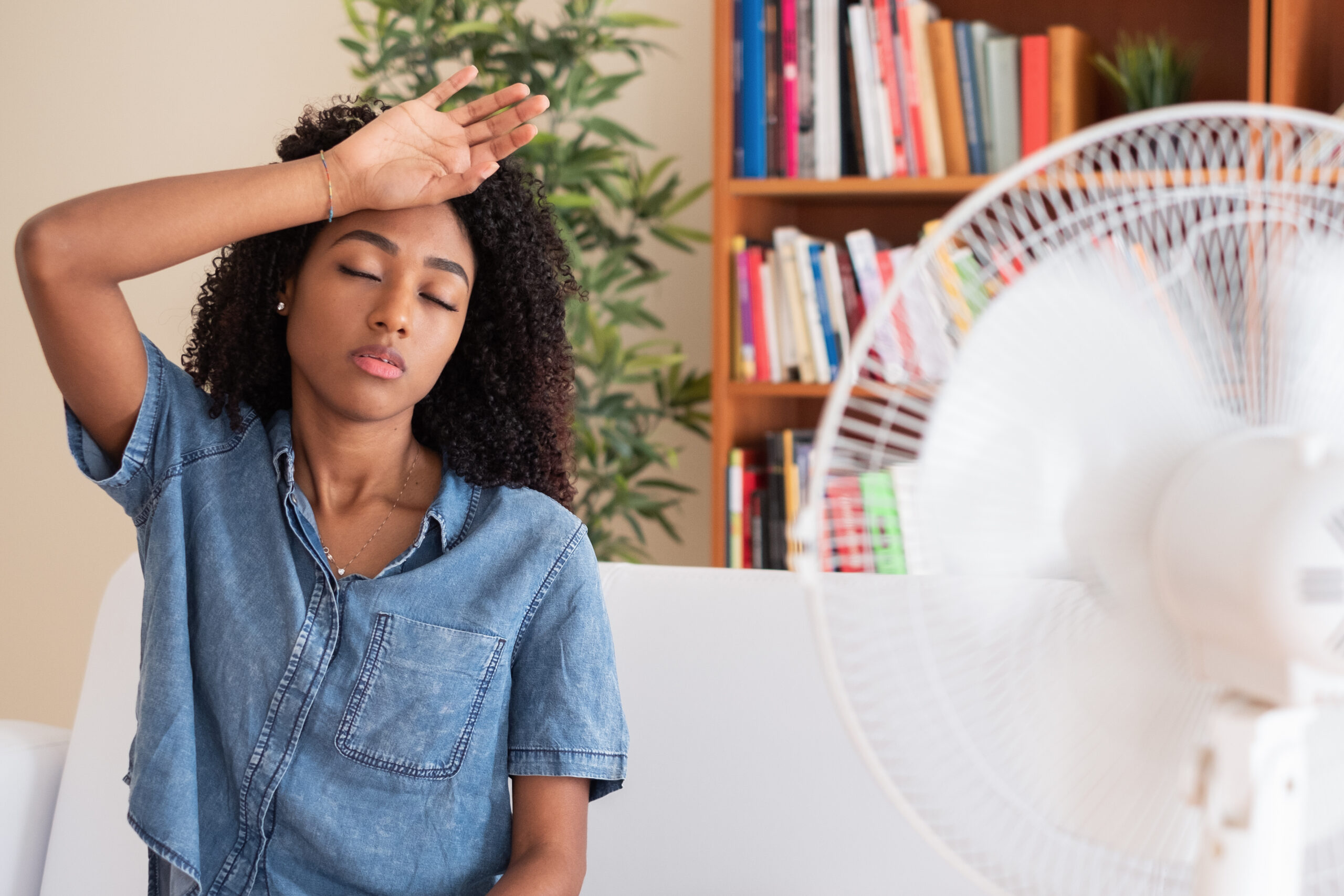 Woman trying to cool down in front of a fan because her air conditioning isn’t working properly