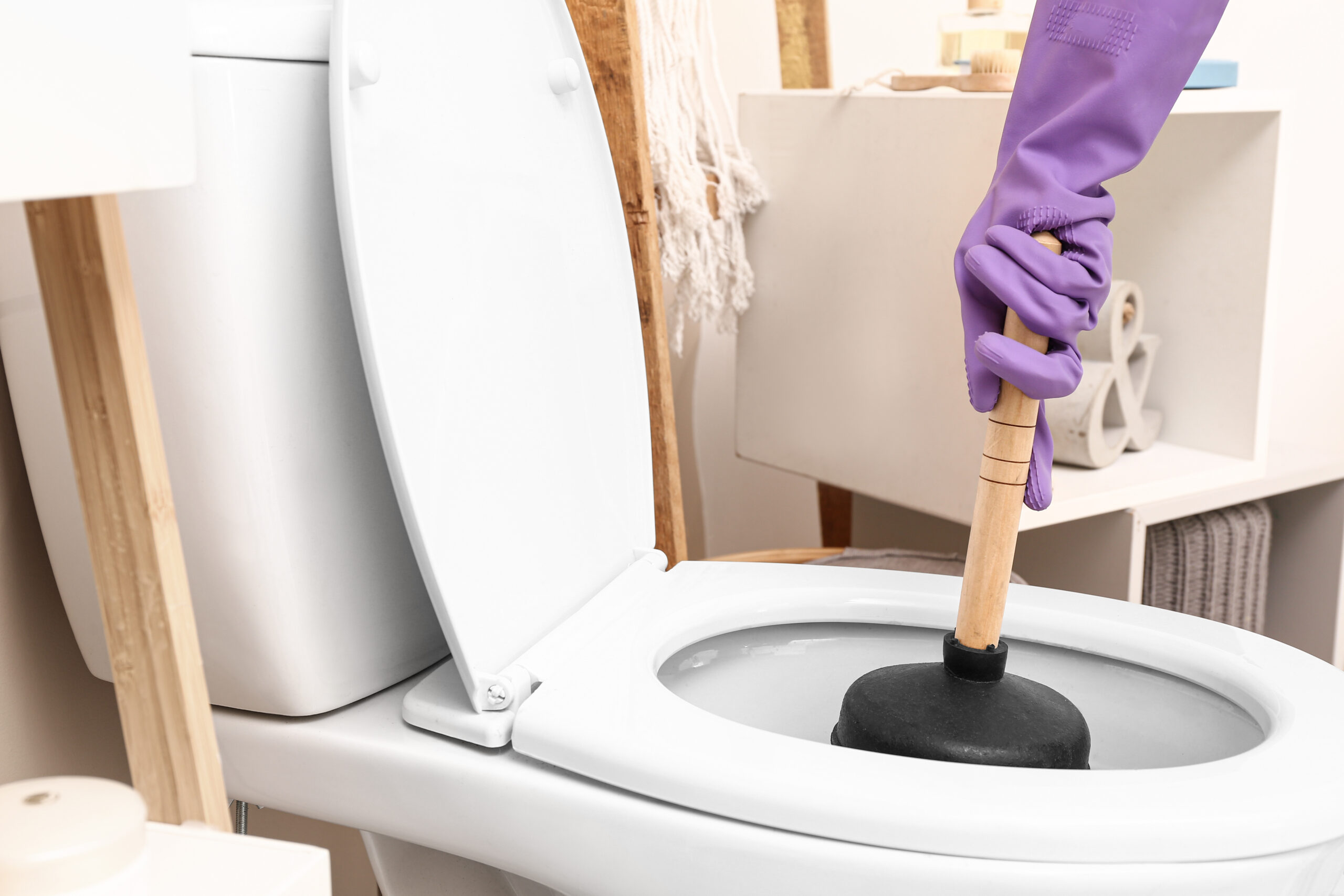Person wearing a purple glove using plunger to unclog toilet.