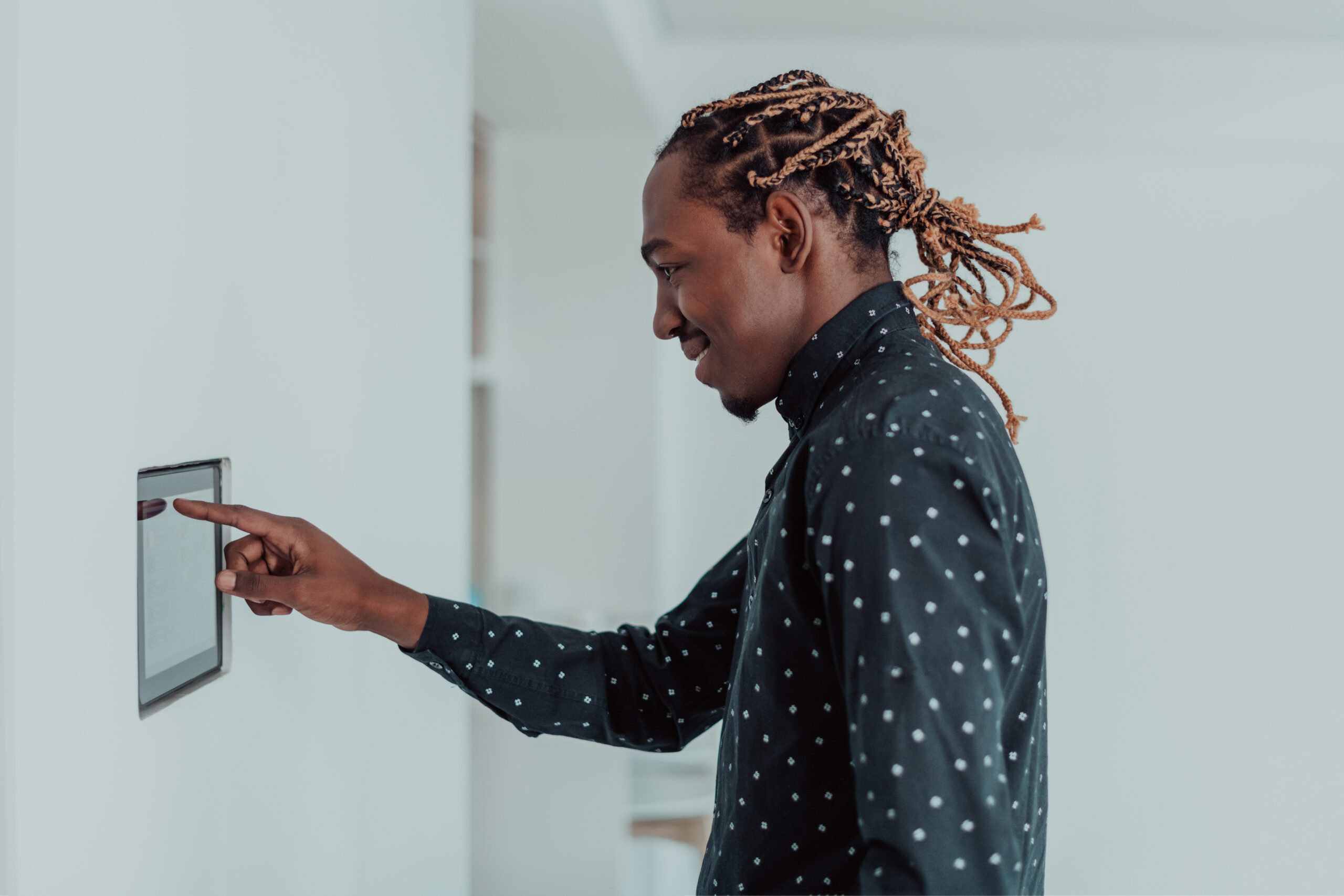 Smiling man using modern smart home system controller on wall