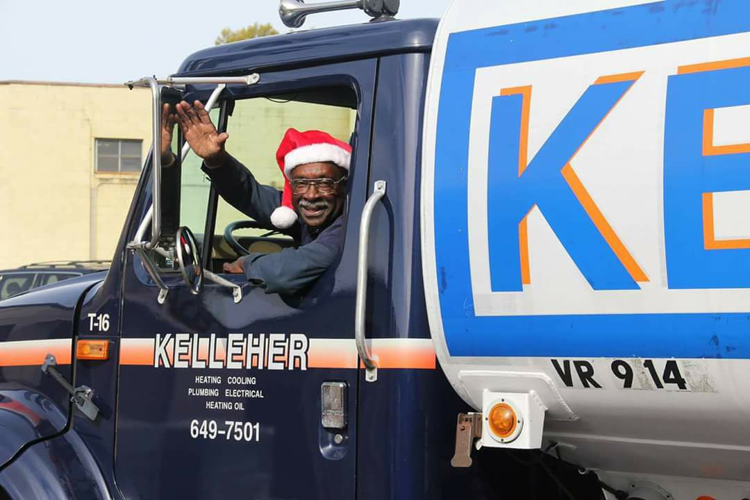 Kelleher professional wearing a Santa hat, smiling and waving in the driver’s seat of a Kelleher heating oil truck heading out to a job