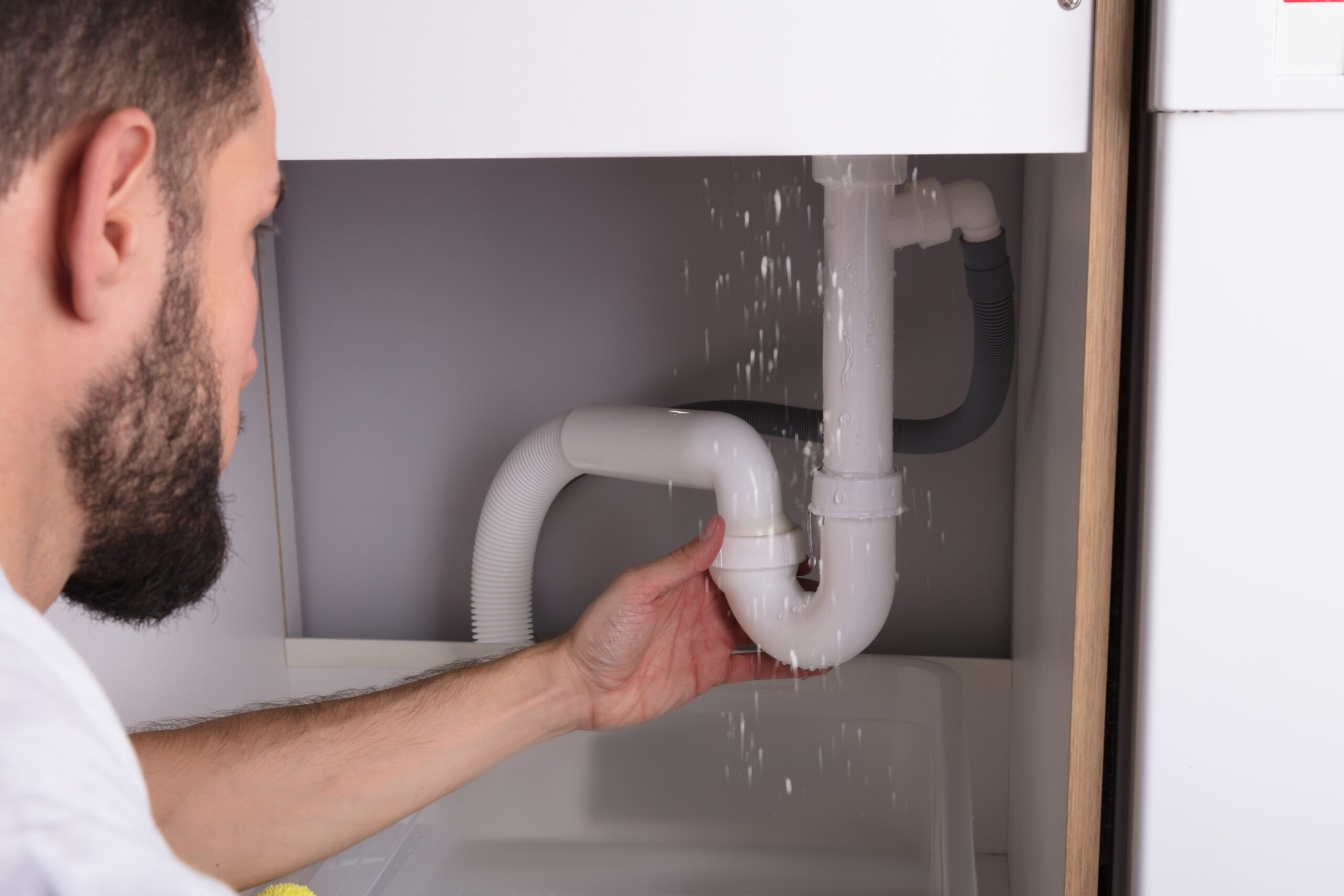 Man Looking At Sink Pipe Leakage needs to call a professional plumber
