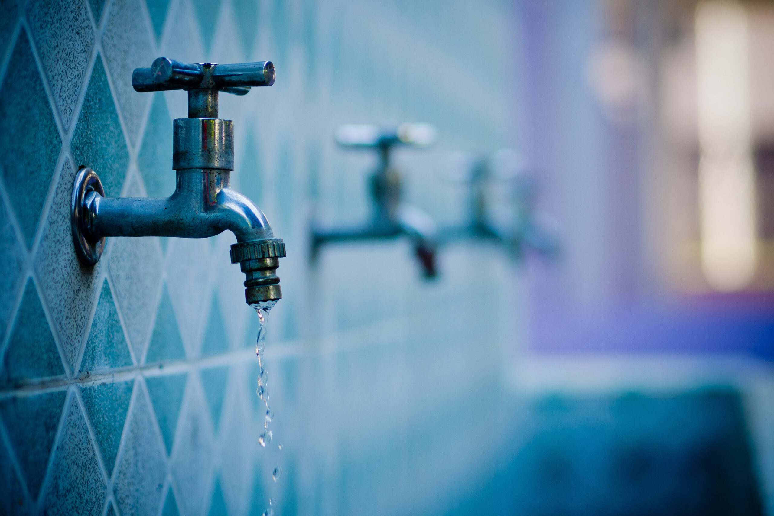 Old water faucet, leaking water on blue tiled wall