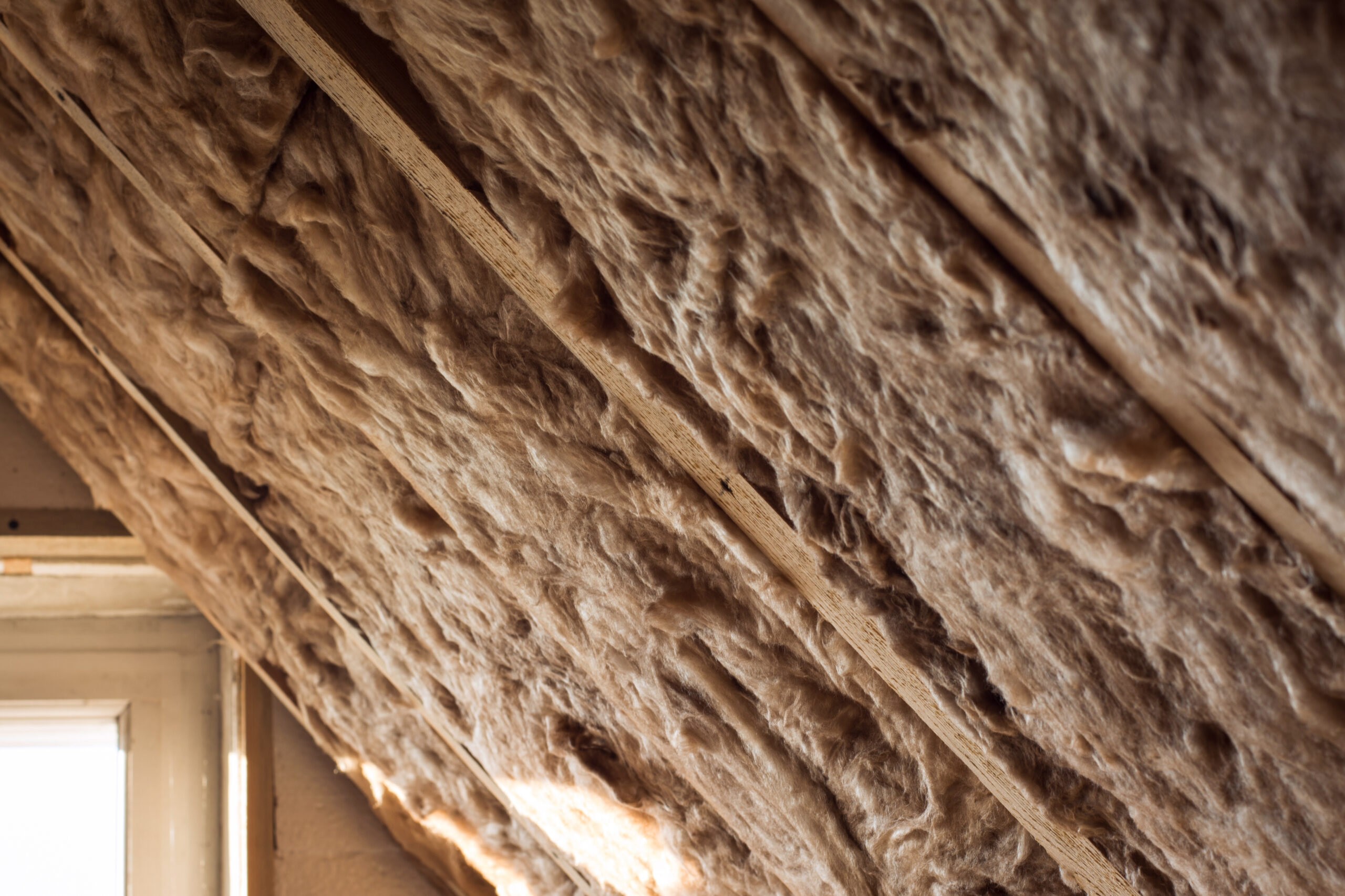 Glass wool and styrofoam insulation in a wooden frame on a inclined attic wall near a window