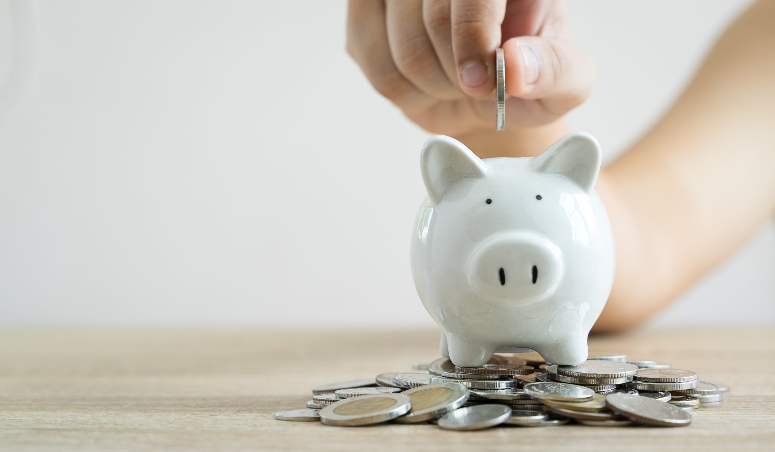 Money savings concepts hand holding coin to put in piggy bank to spend on expenses such as savings, tourism, investment, emergency, retirement on wooden table with blur background