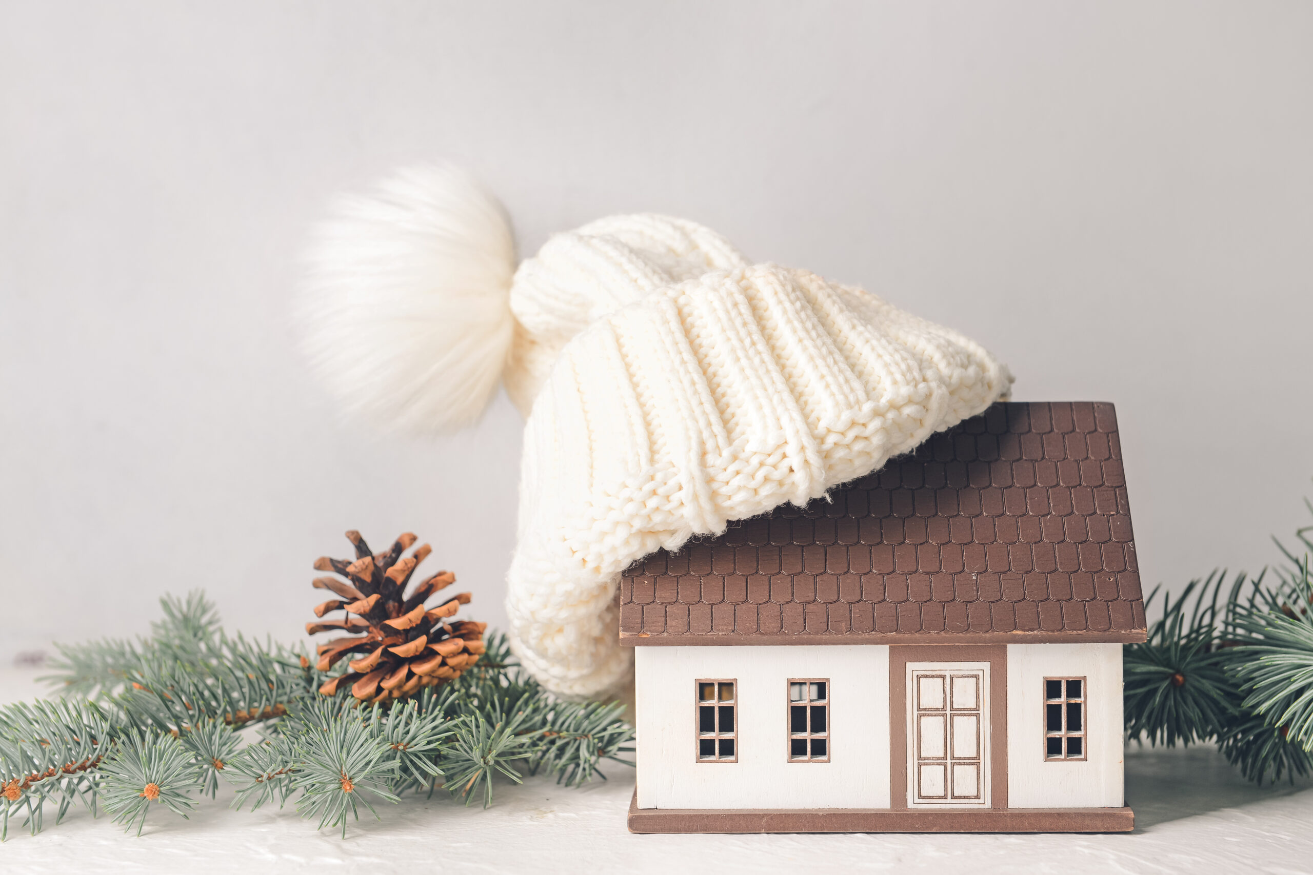 Figure of house and warm hat on table with pine garland. Concept of heating season