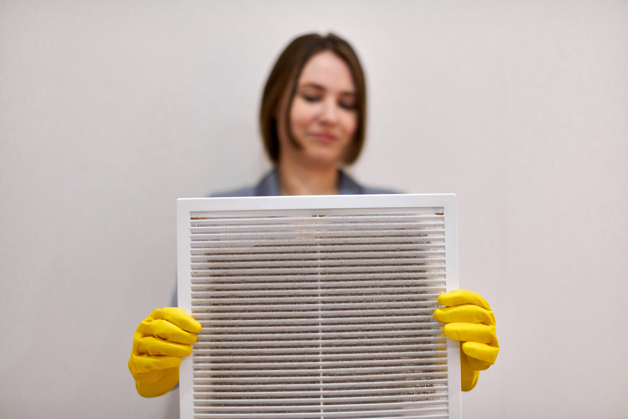 Woman wearing yellow gloves, holding dirty old air filter.