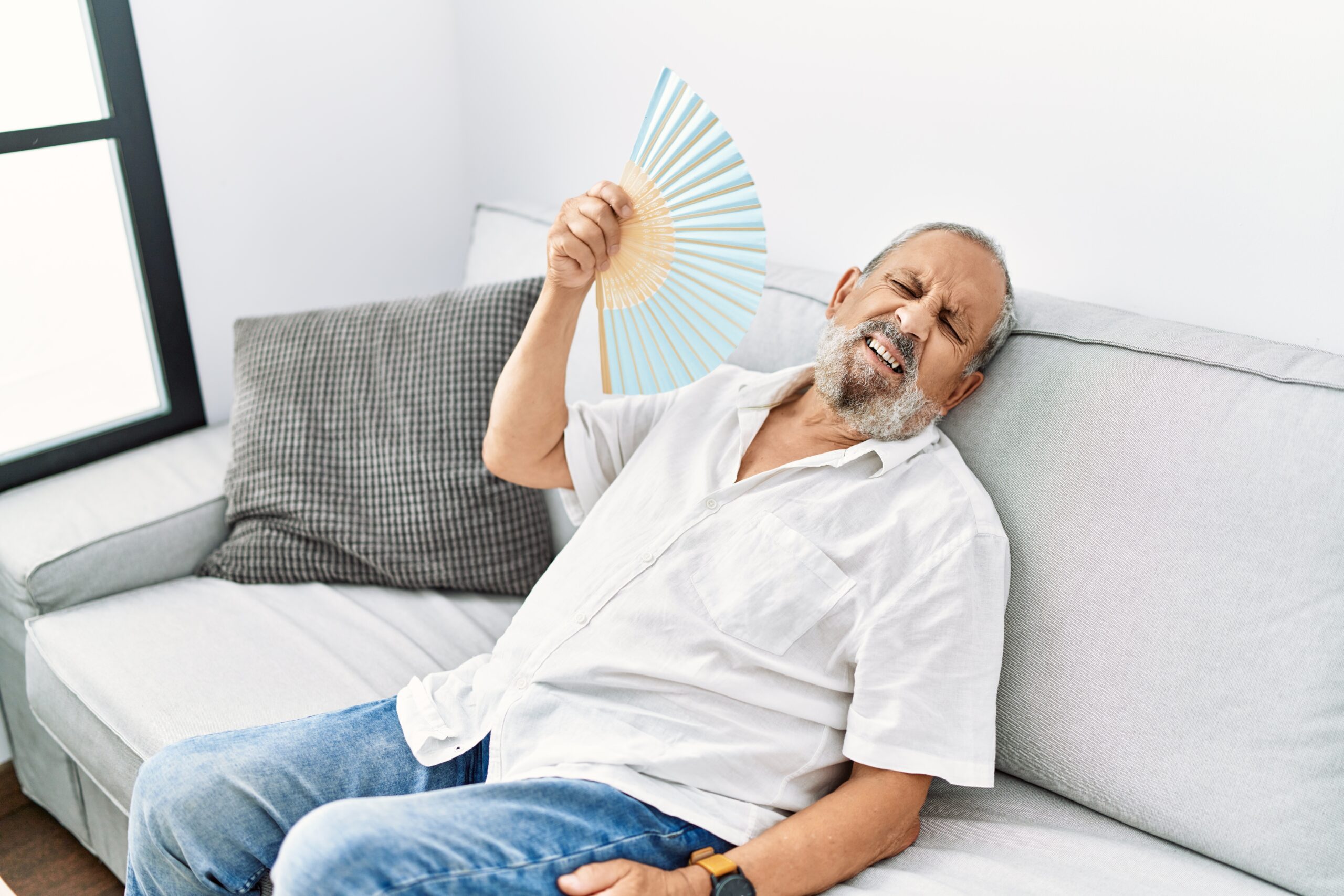 Senior grey-haired man using handfan at home because his AC is broken