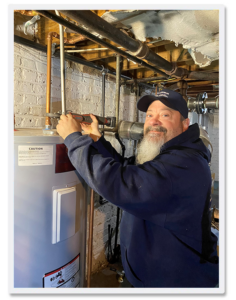 Lonnie from Kelleher HVAC installs a water heater in a basement, using a wrench on copper piping.